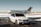 A luxurious car and private jet are parked on a snowy runway. The car, a silver BMW with tinted windows, is in front of the sleek, white aircraft. The setting is an airfield with patches of snow on the ground under a clear sky.
