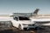 A luxurious car and private jet are parked on a snowy runway. The car, a silver BMW with tinted windows, is in front of the sleek, white aircraft. The setting is an airfield with patches of snow on the ground under a clear sky.