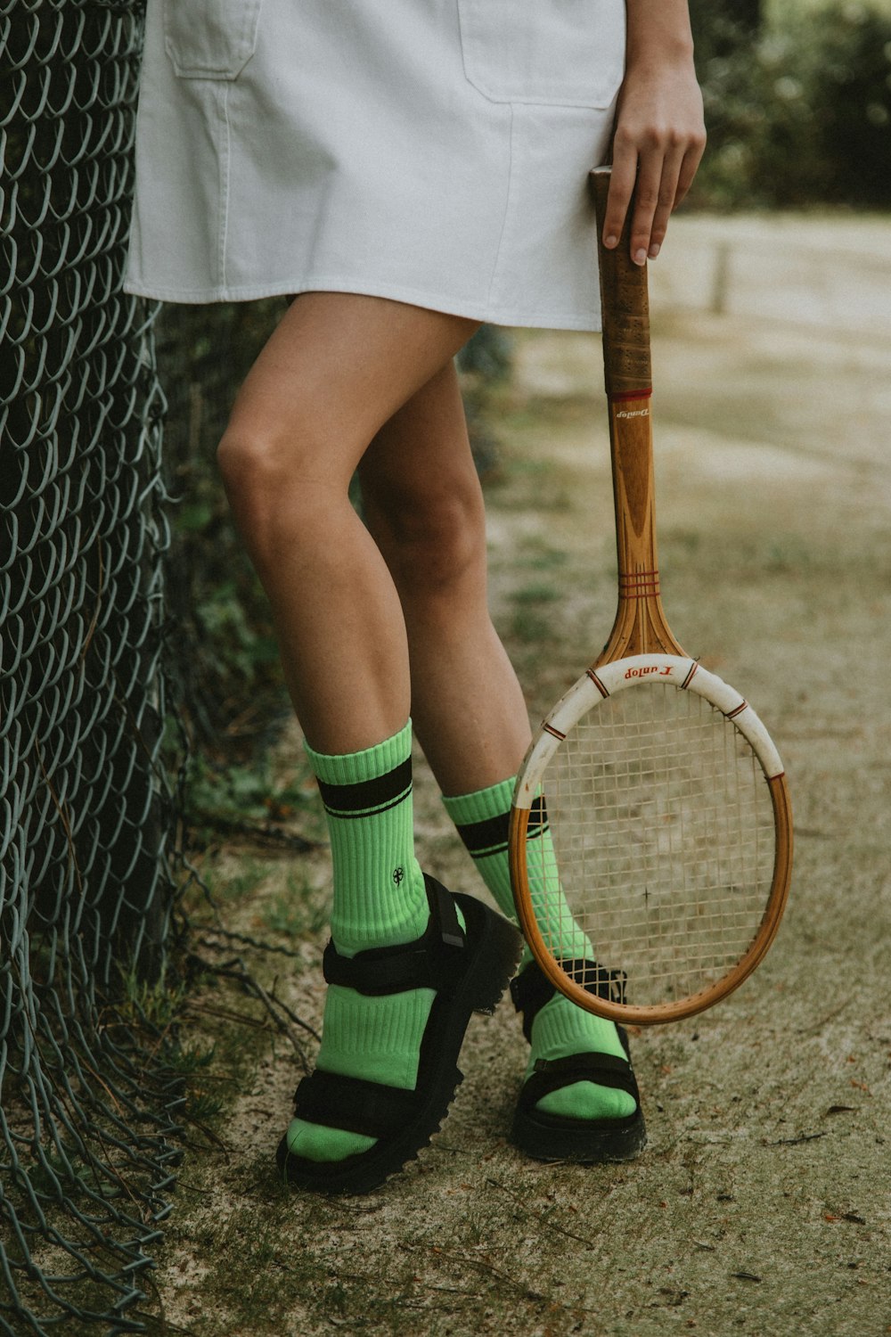 woman in white skirt and green socks holding brown and white tennis racket