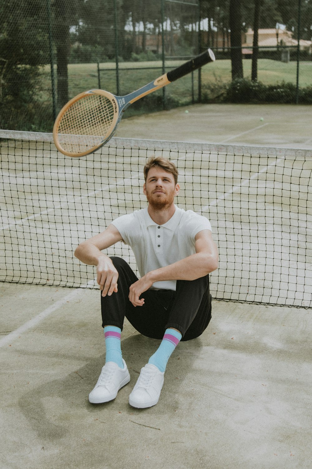 man in white polo shirt and black pants sitting on tennis court