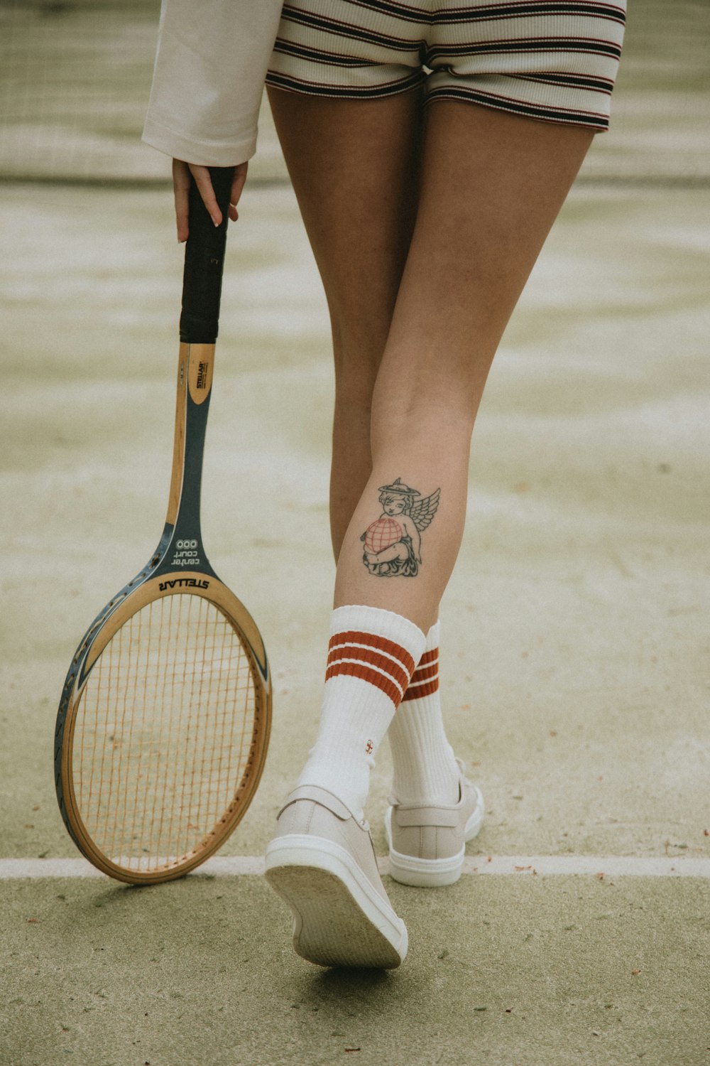 Frau in weißen und roten Socken und weißen Lederschuhen mit braunem und schwarzem Tennisschläger