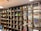 A large wooden shelf with grid-like compartments filled with various objects including figurines, model vehicles, plants, and art supplies. The top section features mannequin-like figures. The shelf is part of a well-lit room with a clean and organized appearance.