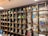 A large wooden shelf with grid-like compartments filled with various objects including figurines, model vehicles, plants, and art supplies. The top section features mannequin-like figures. The shelf is part of a well-lit room with a clean and organized appearance.
