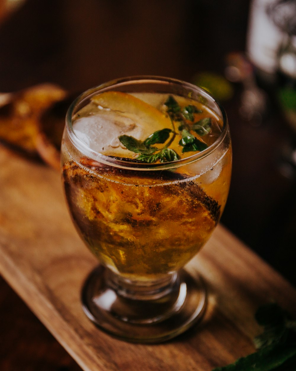 clear drinking glass with brown liquid and green leaves