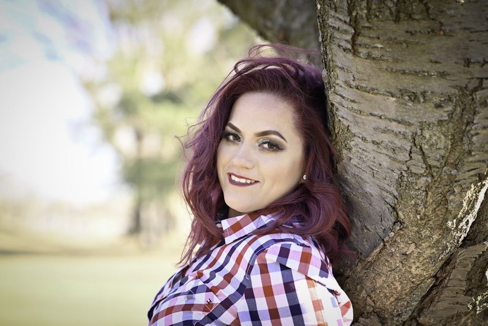 woman in red white and blue plaid dress shirt leaning on brown tree