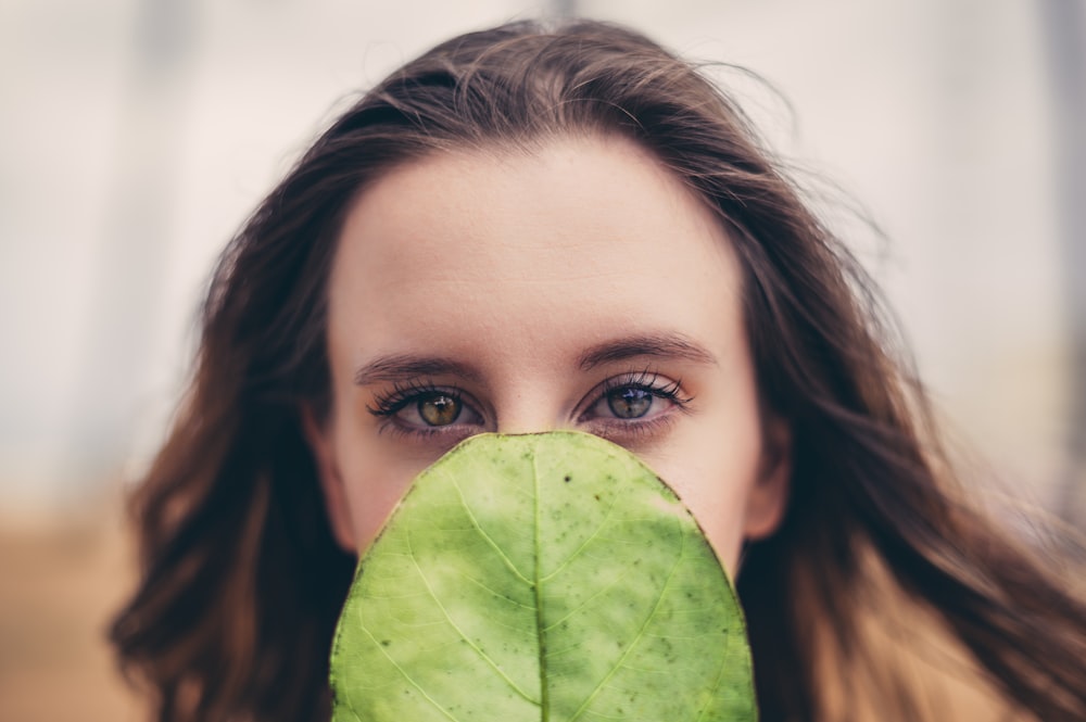 femme couvrant son visage avec une feuille verte