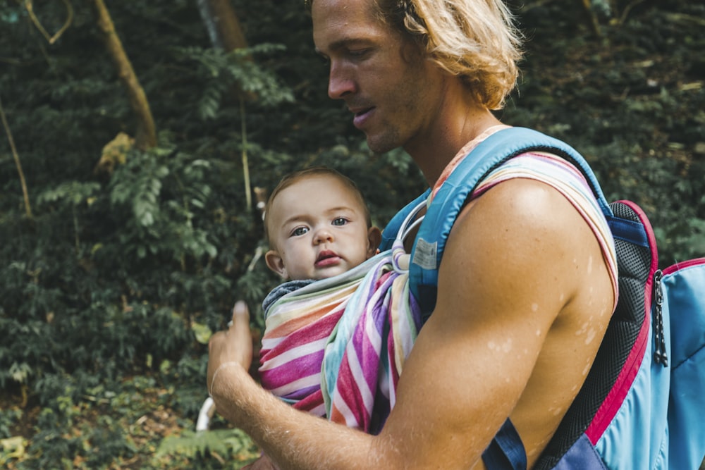 woman in blue tank top carrying baby in pink and white stripe shirt