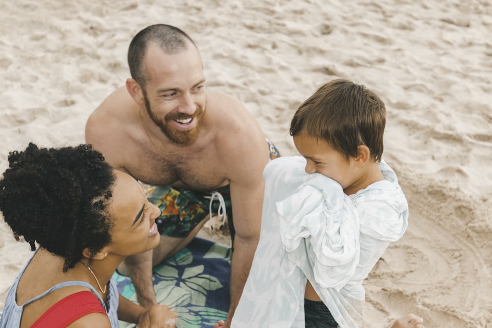 낮 동안 해변에서 빨간색과 흰색 줄무늬 셔츠를 입은 아이를 안고 있는 흰색 반바지를 입은 남자