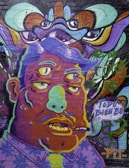 A vivid and surreal mural depicting a character with three eyes and exaggerated facial features. The art style is psychedelic and cartoonish, with bold outlines and a colorful palette. Above, abstract patterns and eyes add a sense of mystery. The character has a cigarette in its mouth, and a speech bubble containing Spanish text, 'TODO BIEN BO'.