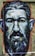 A vibrant street art mural depicting a man's face with detailed expressive features and a beard. The artwork is painted in bold strokes with a mix of colors on a rough textured wall background.