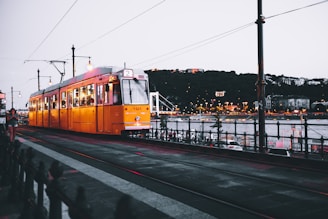 A colorful tram gliding along the Danube River with the Parliament building in the background.