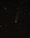 A night sky filled with numerous stars and a prominent visible comet with a glowing tail. There is also a faint streak of light, possibly a meteor, crossing the upper left of the image.