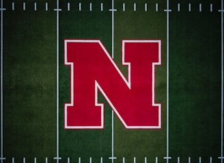 A large red letter 'N' with a white outline is centered on a green football field with white yard lines.