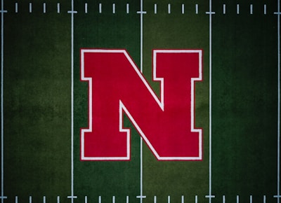 A large red letter 'N' with a white outline is centered on a green football field with white yard lines.