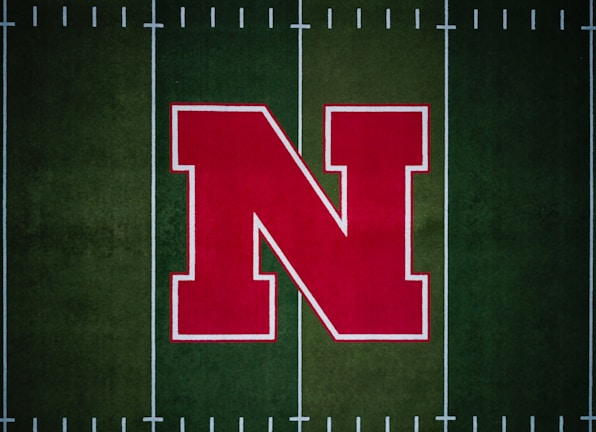 A large red letter 'N' with a white outline is centered on a green football field with white yard lines.