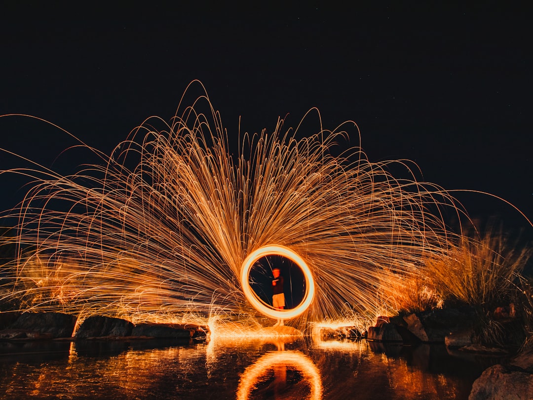 steel wool photography of man standing on the beach during night time