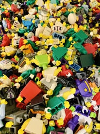 A large pile of colorful plastic toy parts depicting miniature humanoid figures with detachable bodies, heads, and hands. The parts are mixed together in a variety of colors such as red, blue, green, yellow, and black.