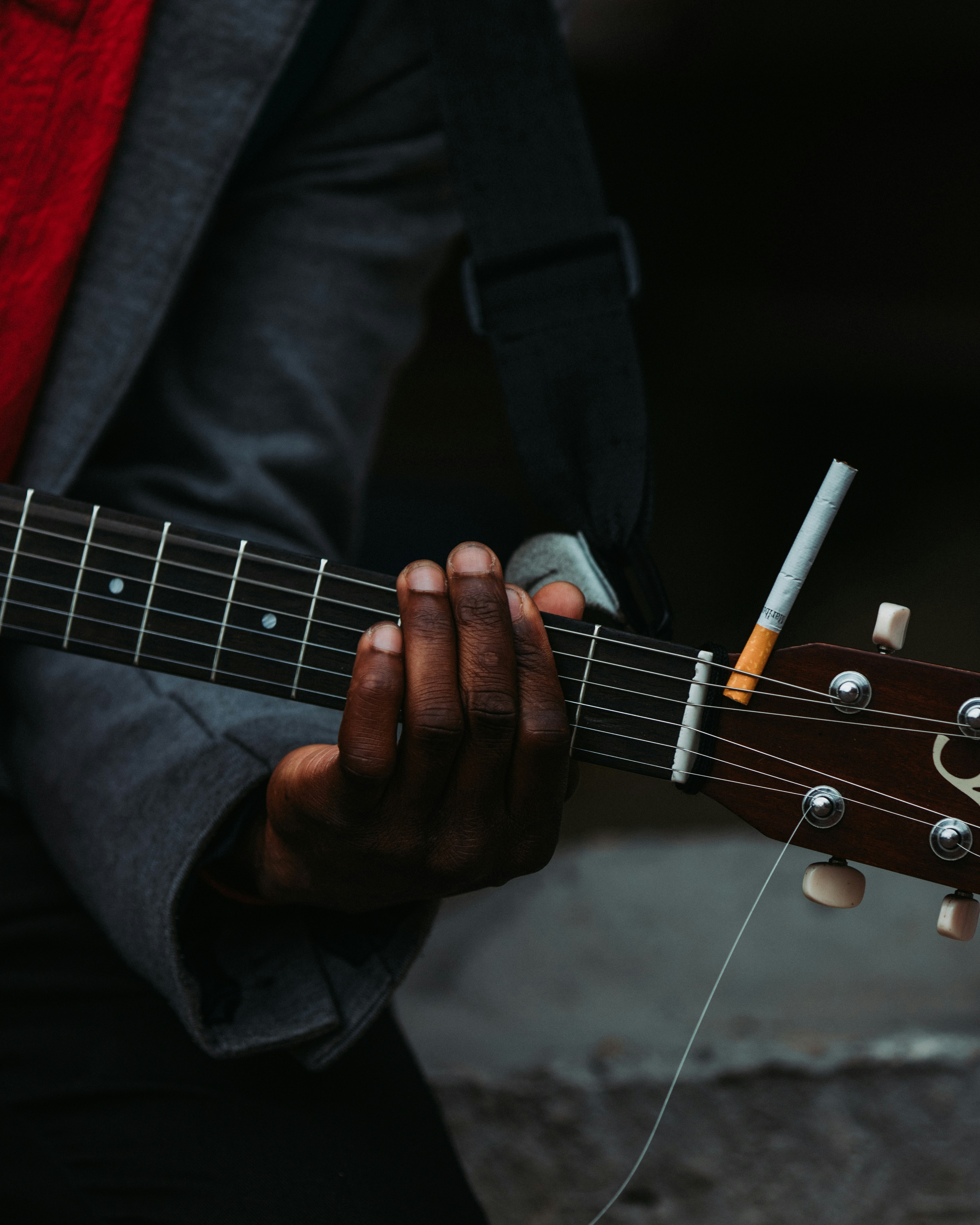 Hånd der trykker på guitarstrenge med en cigaret liggende ved siden af.
