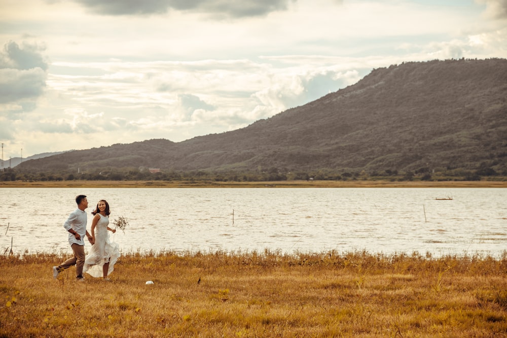 woman in white dress sitting on green grass field near lake during daytime