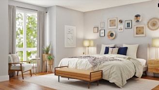 A beautifully decorated bedroom features a large bed with white and beige linens, accented by dark blue and patterned pillows. Above the bed is an arrangement of various framed artworks and decorative plates on the wall. A wooden bench sits at the foot of the bed. To the left, a cozy armchair with a pillow is placed beside a window with long, light-colored curtains allowing natural light to brighten the room. Beside the chair, a small round side table holds a couple of books and a plant. Another plant in a decorative pot is positioned next to a wooden bedside table, complemented by a modern lamp.