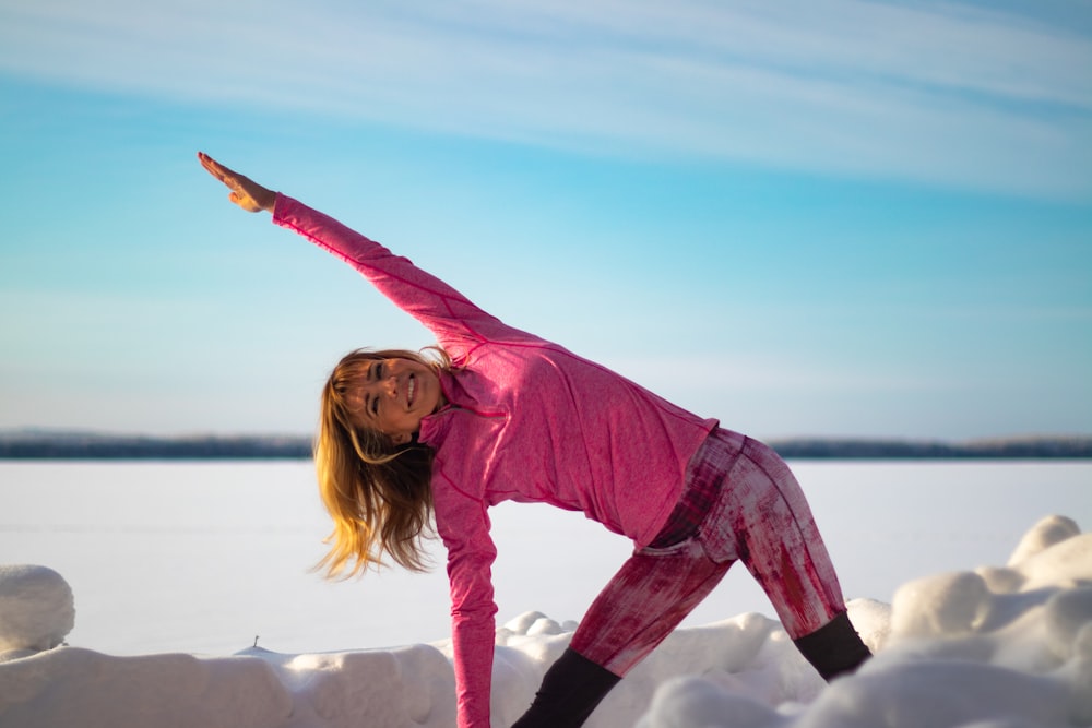 woman in pink long sleeve shirt and black pants standing on white rock during daytime