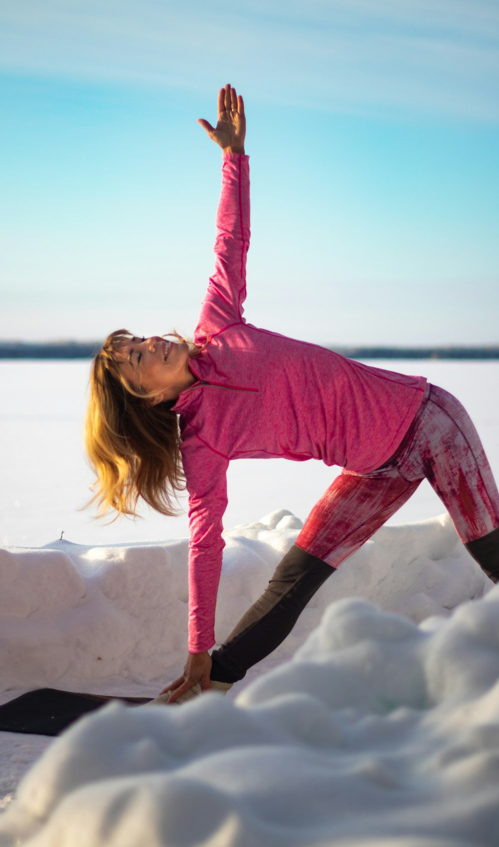 woman in pink long sleeve shirt and black pants sitting on white snow covered ground during
