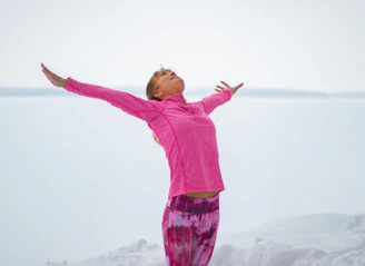 girl in pink long sleeve shirt and purple pants standing on white snow covered ground