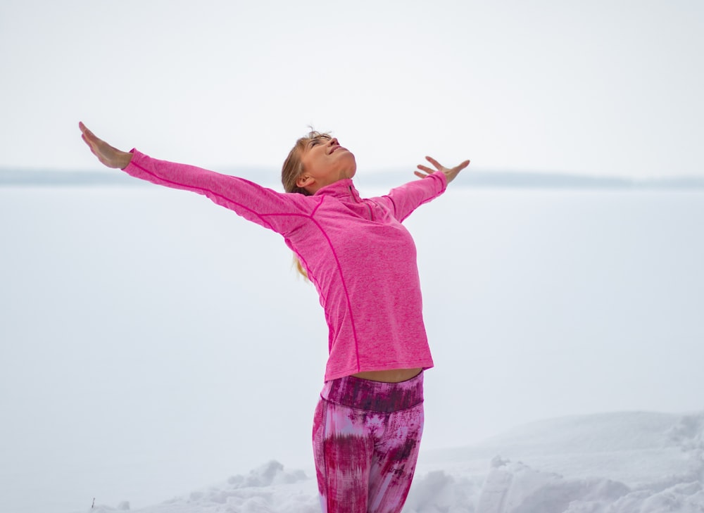 girl in pink long sleeve shirt and purple pants standing on white snow covered ground