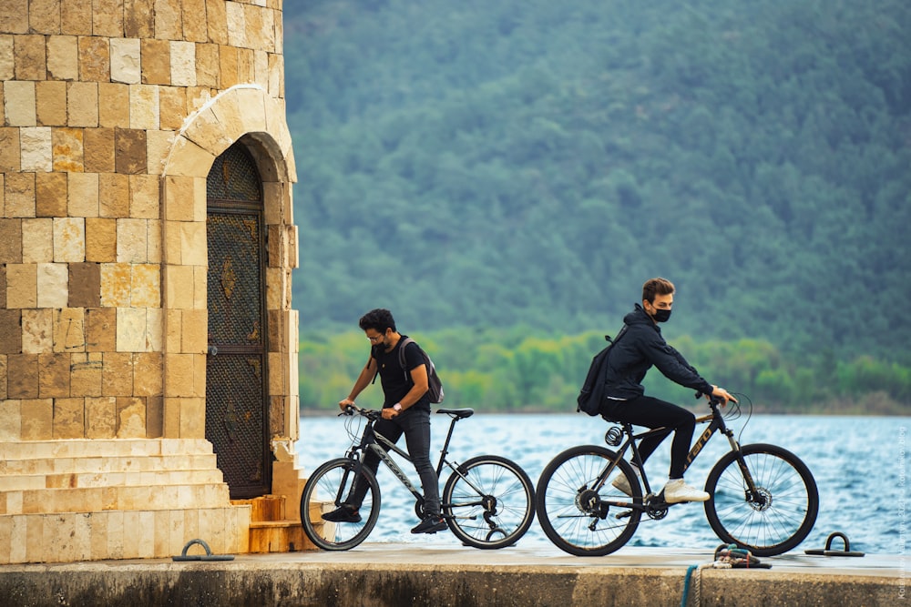 a couple of men riding bikes next to a body of water