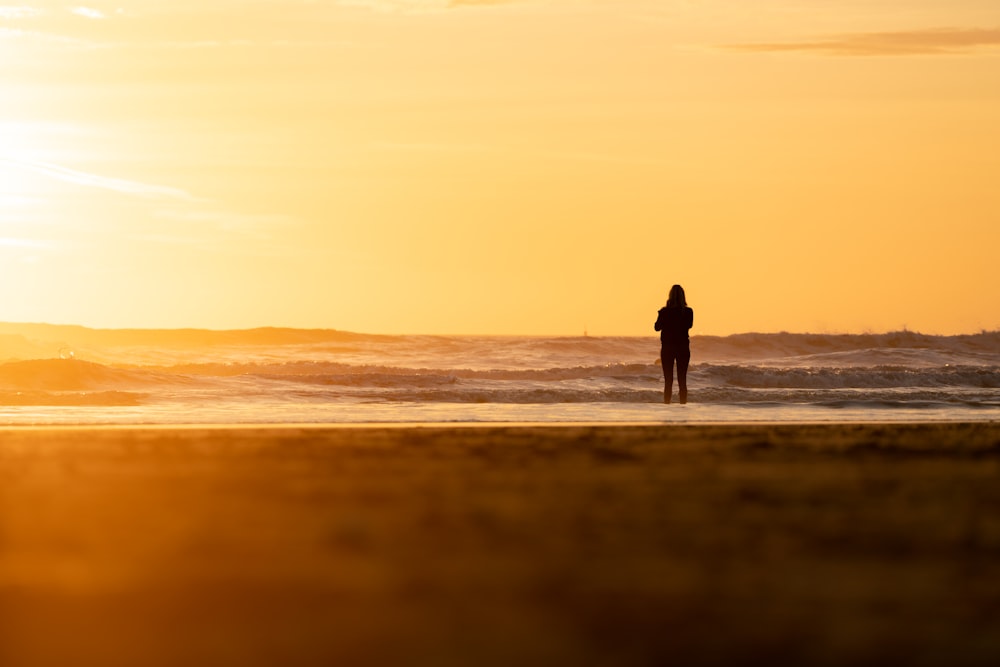 Silhouette von Mann und Frau, die während des Sonnenuntergangs am Strand spazieren gehen