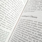 An open physics book showing Feynman diagrams with colorful annotations.