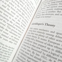 A close-up view of an open book displaying text. The title 'Schrödinger's Theory' is prominently featured, surrounded by content discussing matrix mechanics and quantum theory. The pages are filled with dense text in a formal typeface.