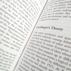 A close-up view of an open book displaying text. The title 'Schrödinger's Theory' is prominently featured, surrounded by content discussing matrix mechanics and quantum theory. The pages are filled with dense text in a formal typeface.