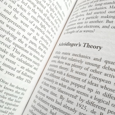 A close-up view of an open book displaying text. The title 'Schrödinger's Theory' is prominently featured, surrounded by content discussing matrix mechanics and quantum theory. The pages are filled with dense text in a formal typeface.
