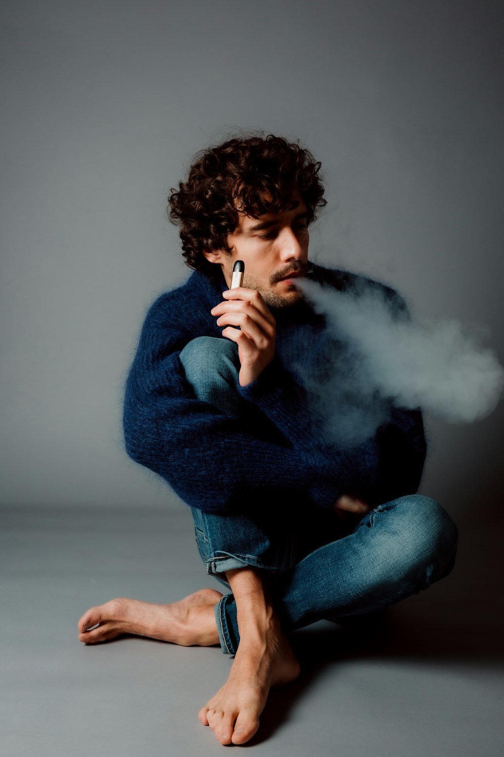 man in blue sweater smoking cigarette