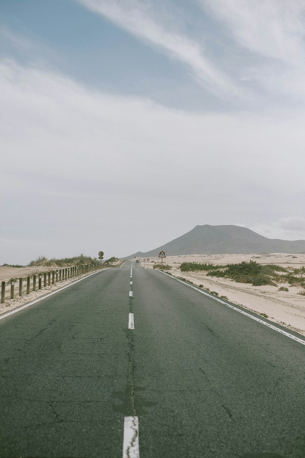 gray asphalt road between green grass field under white sky during daytime