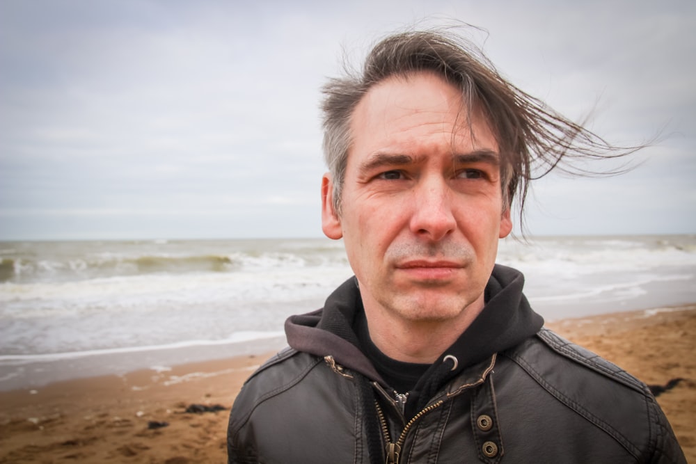 man in black zip up jacket standing on beach during daytime