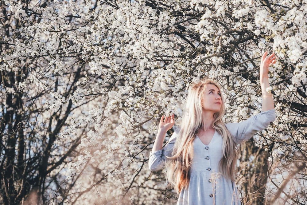 woman in white long sleeve shirt standing beside white cherry blossom tree during daytime
