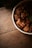 A bowl filled with chunks of pork belly, possibly braised, is placed on a rustic wooden table. The meat appears succulent and is garnished with green herbs, creating a homely and appetizing presentation.