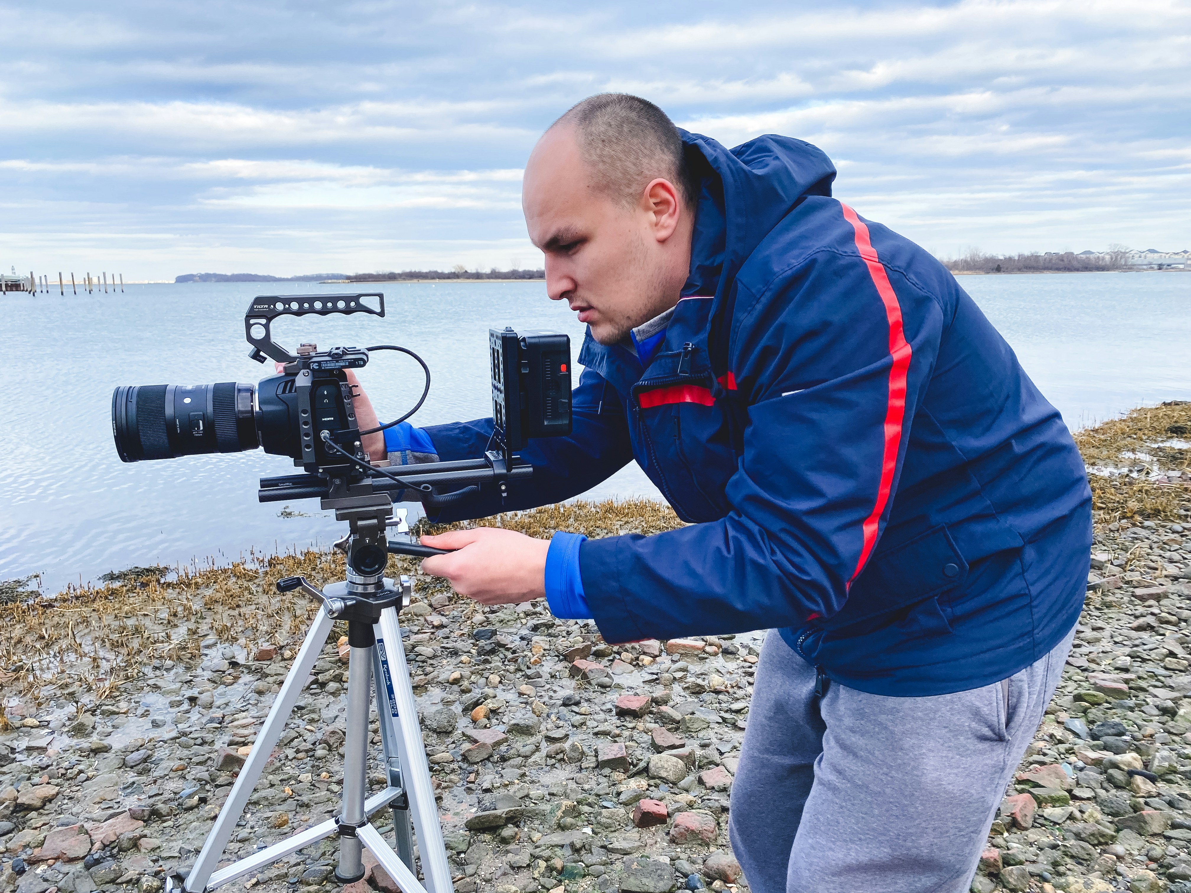 boy in red and blue jacket holding black camera on tripod