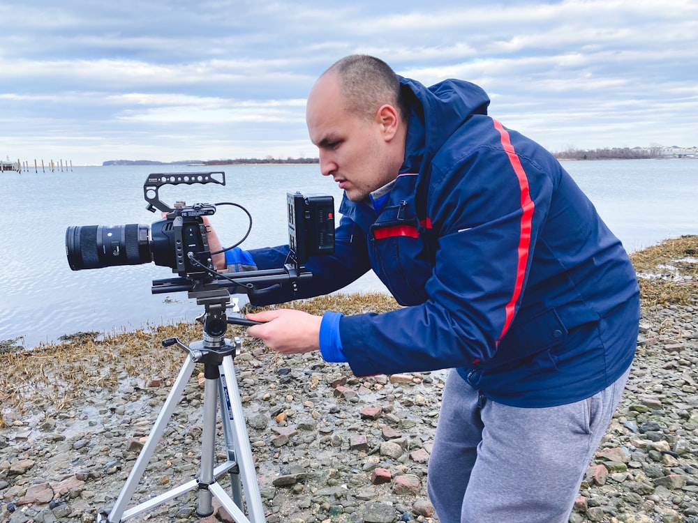 boy in red and blue jacket holding black camera on tripod