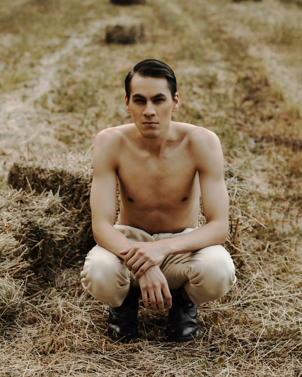 topless man in black pants sitting on brown grass field during daytime