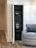 A neatly organized server rack is positioned within a recessed area of a room. The rack holds various electronic equipment, including amplifiers, switches, and other audio-visual components. The room features a wooden floor and white paneled walls. A gray upholstered armchair is placed nearby, adding a homey touch to the setting.