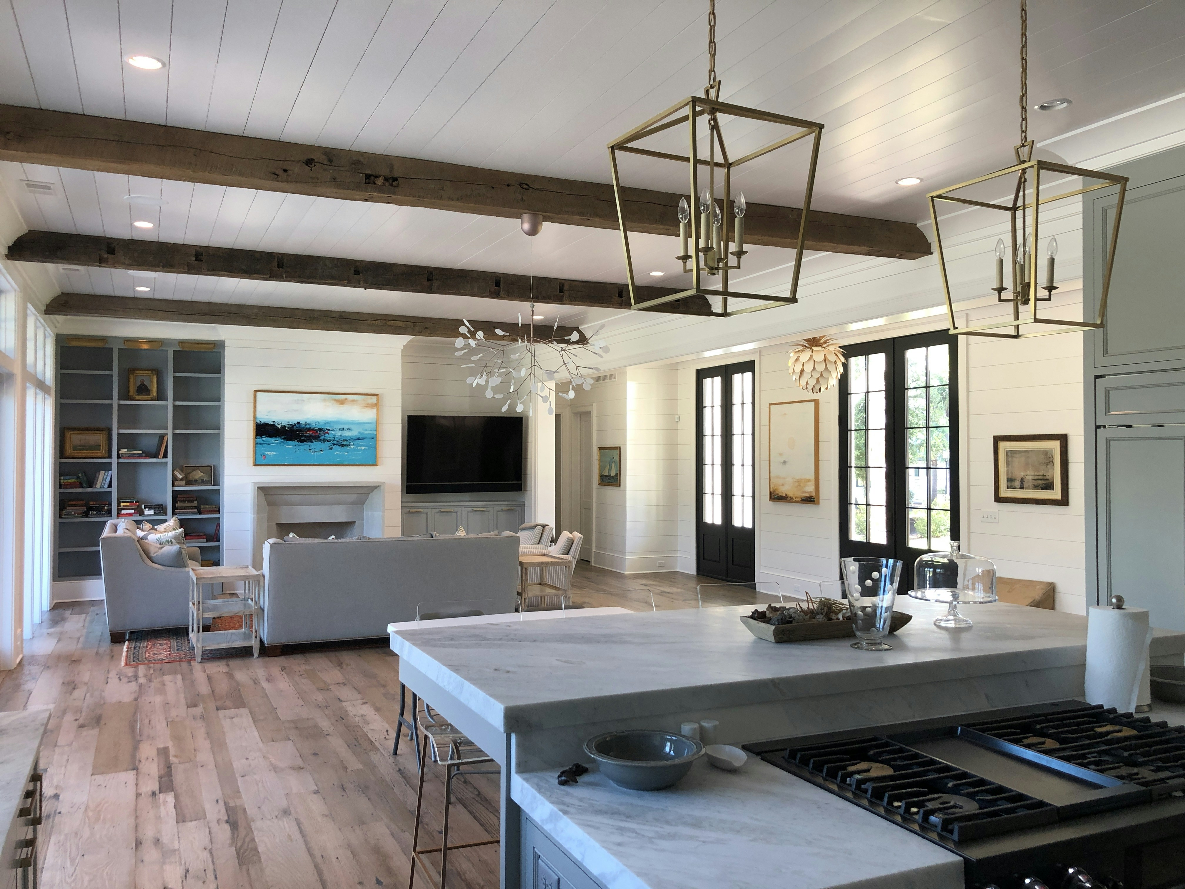 Bright airy craftsman home interior with exposed wood beams, large windows flooding the space with natural light, open floor plan with warm oak hardwood floors