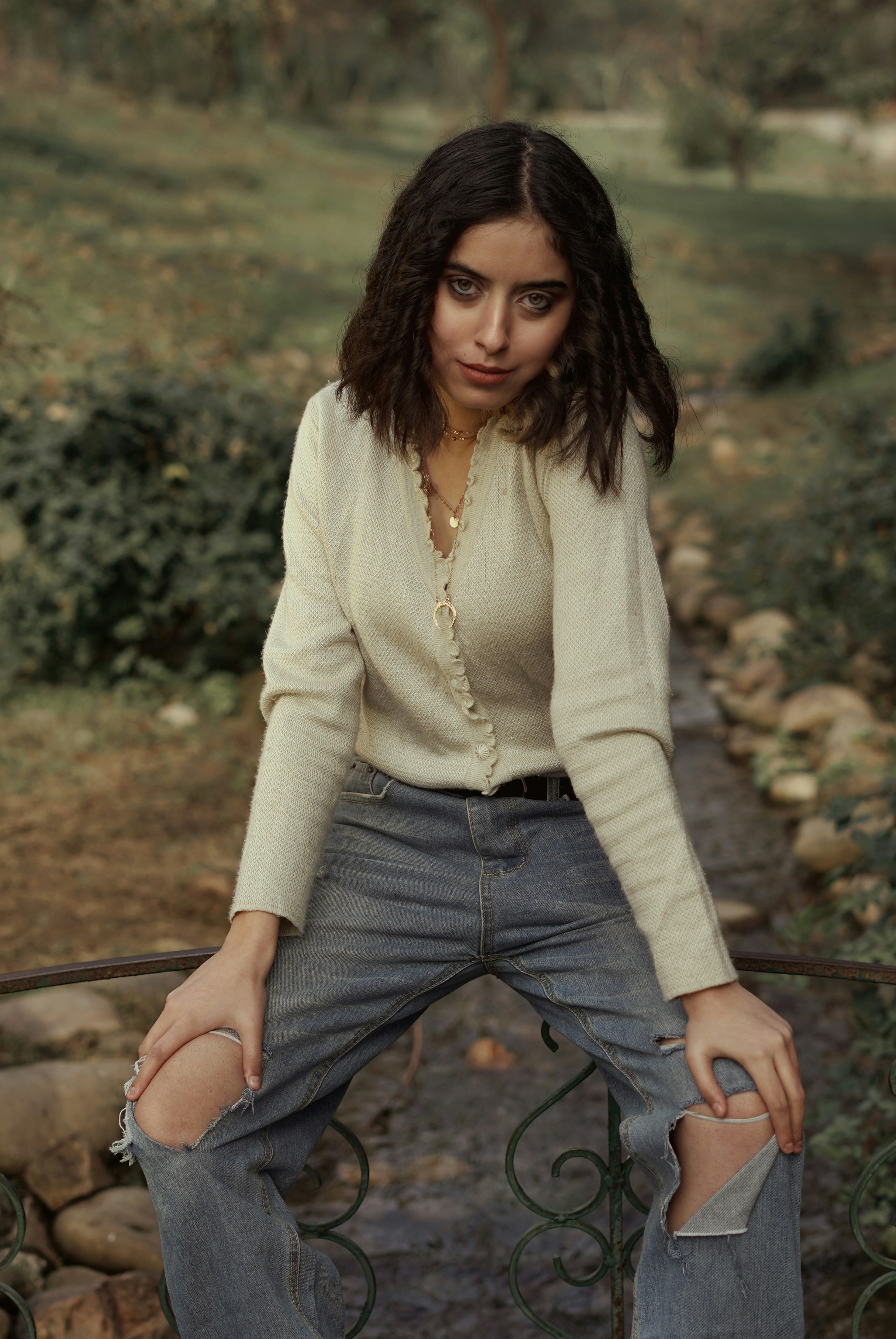 donna in cardigan bianco e jeans blu in denim seduta su ringhiere metalliche nere durante il giorno