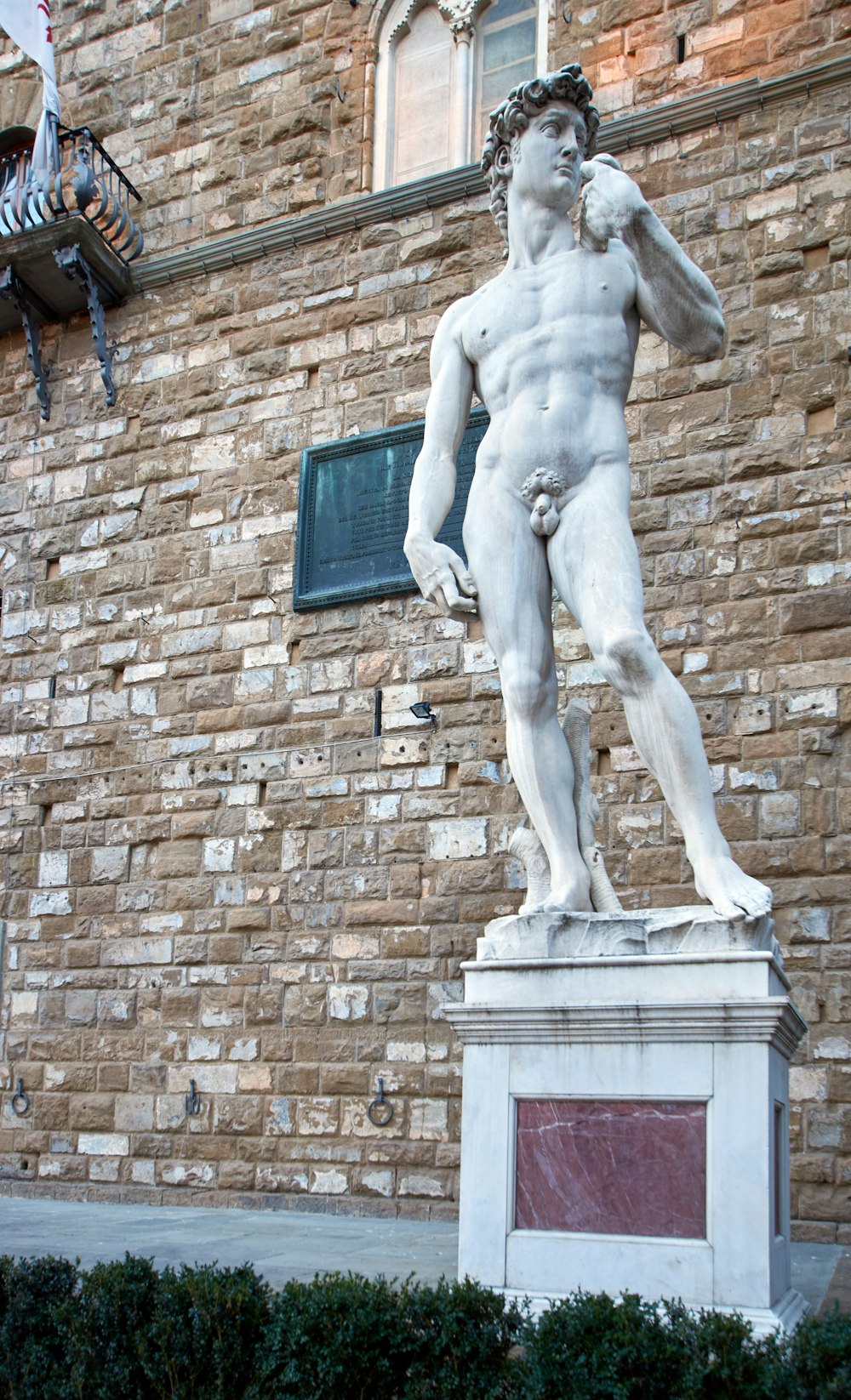 Statue des Menschen auf brauner Ziegelmauer