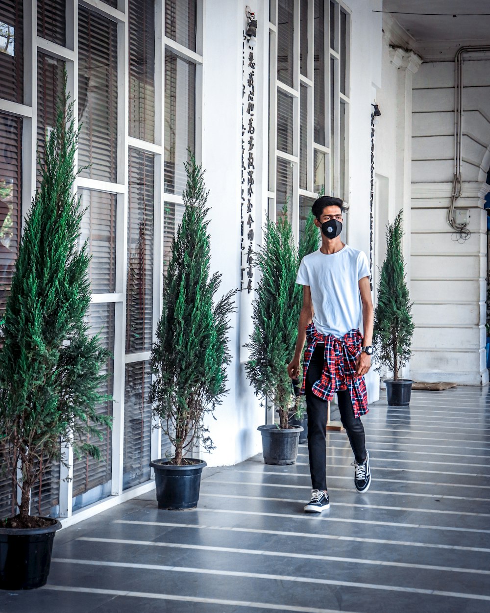 man in white crew neck t-shirt and black pants standing beside green plant during daytime