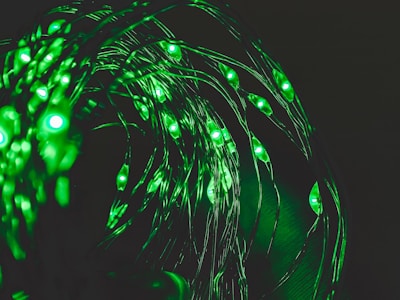A series of glowing green LED lights are intertwined with thin, flexible wires, creating a swirling pattern against a dark background.
