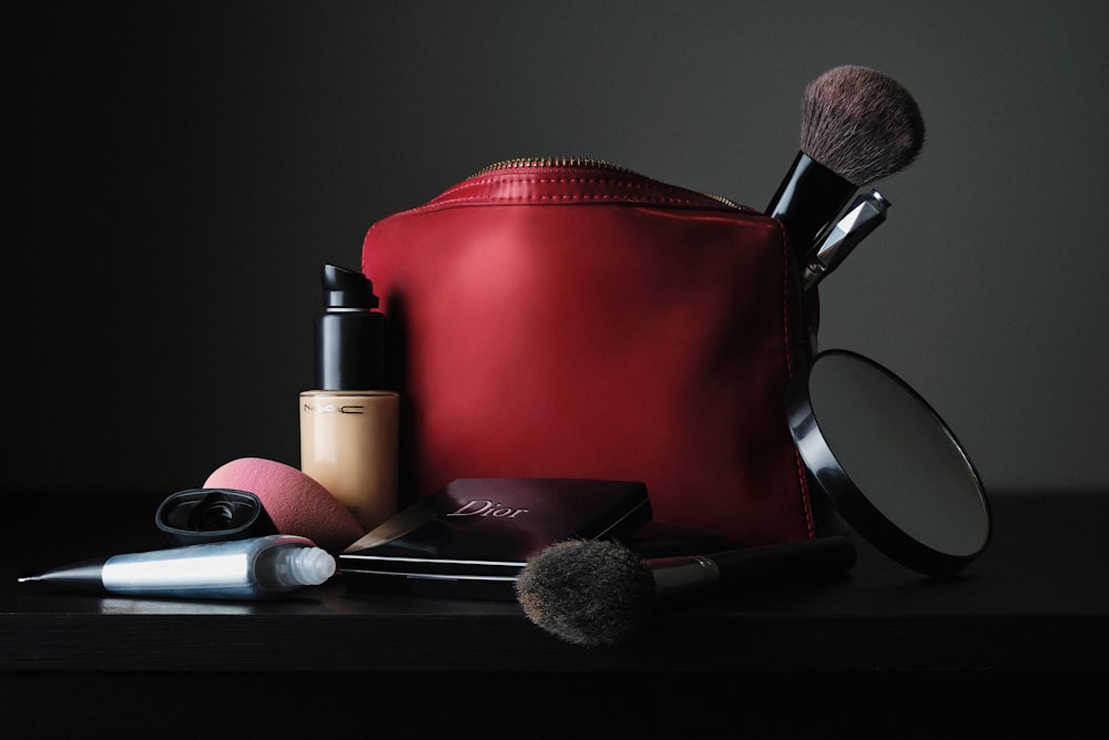 Sac en cuir rouge à côté du pinceau de maquillage noir