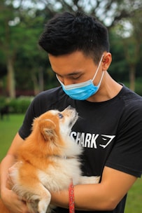 man in black crew neck t-shirt holding brown long coated small dog
